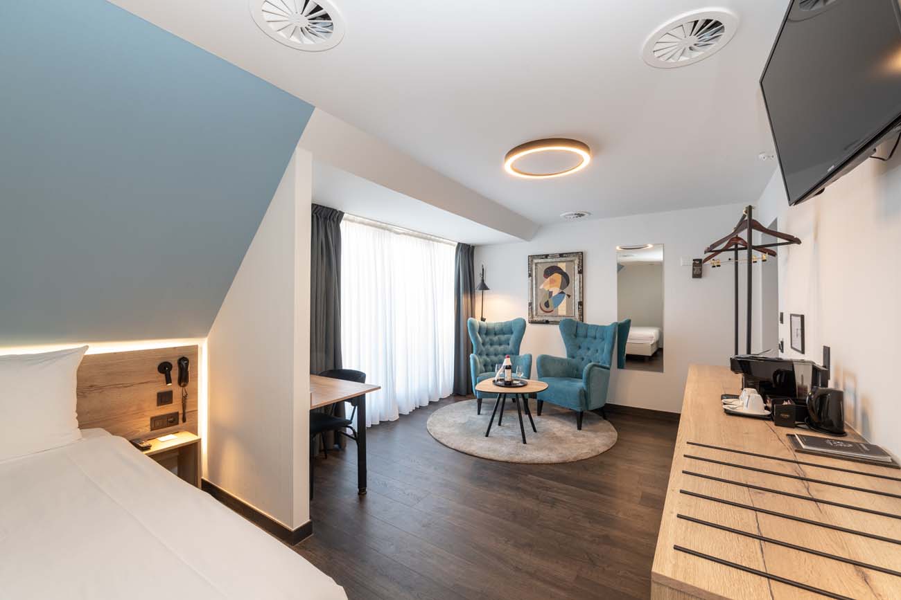 Luxe hotelsuite met slaapkamer, loungegedeelte, turquoise stoelen en moderne verlichting.